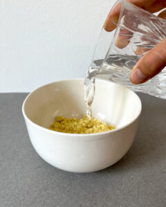 In eine weiße Schale mit dem Terra Vegane Omelett Pulver wird aus einem Gals Wasser eingegossen.